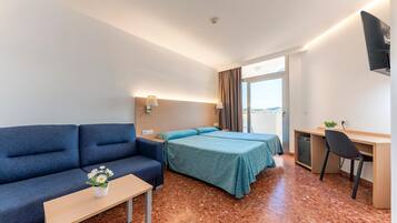 Een hotelkamer met een bank, twee bedden, een bureau, een stoel en een bijzettafeltje met een bloevas.