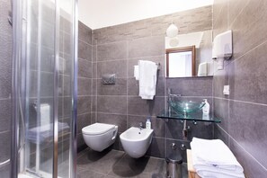 A modern bathroom with a glass shower enclosure, a bidet, a glass sink, and a towel rack. - Maria Rosaria Bed & Breakfast (Ladispoli)