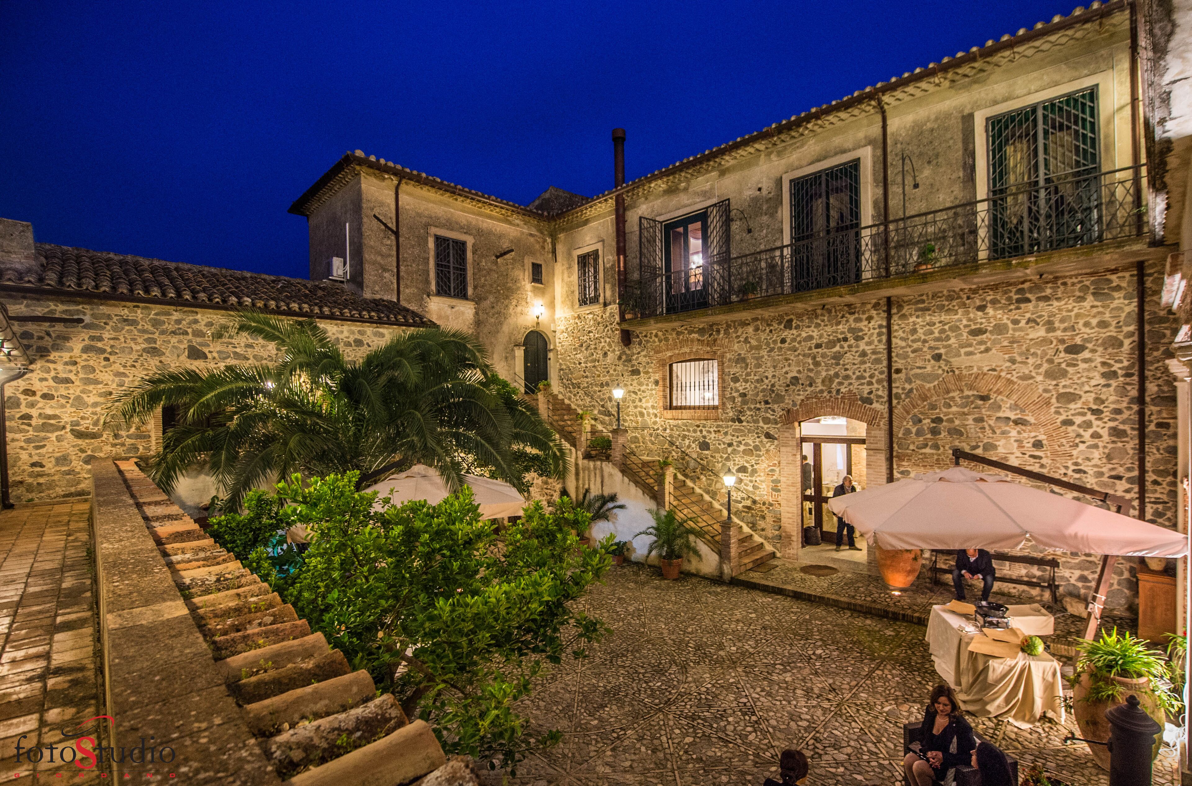 Un patio con edificios de piedra, una escalera y mobiliario exterior con sombrillas.