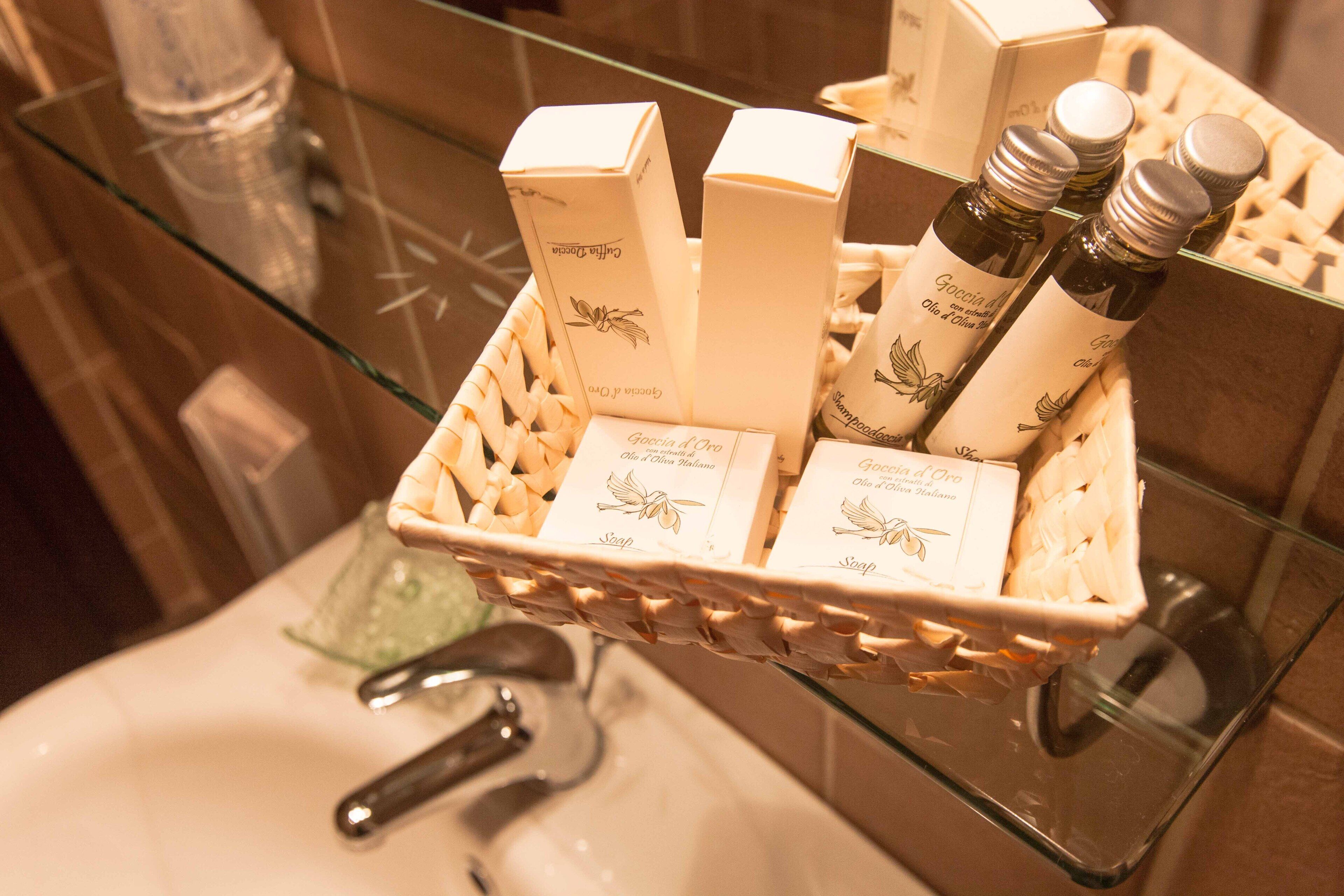 A bathroom with a glass sink, a white soap dispenser, and a wicker basket containing toiletries.