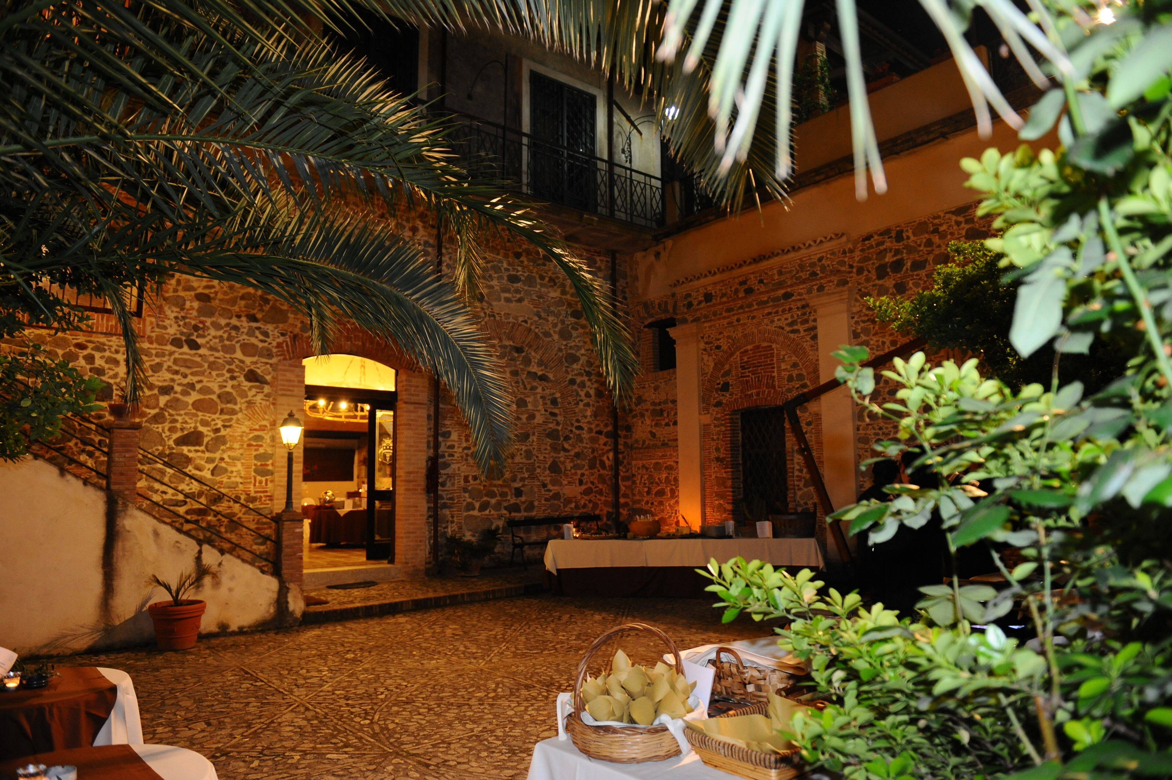An outdoor courtyard with stone walls, a palm tree, and a table with baskets of fruit.