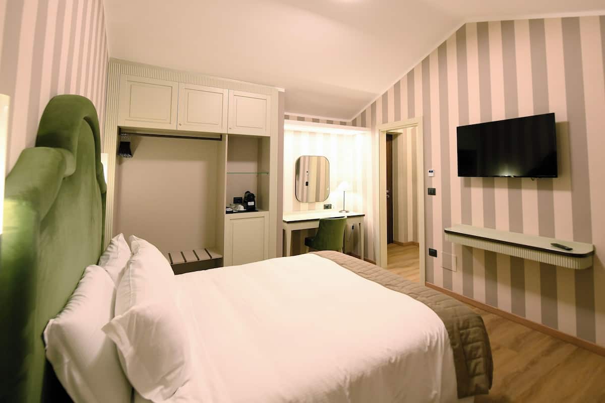 A bedroom with a bed, a desk, a chair, a wardrobe, a mirror, and a TV mounted on the wall.