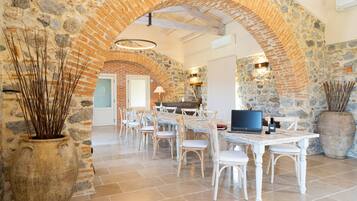 Un comedor amplio con un arco de piedra, sillas blancas y una mesa larga con un ordenador portátil.