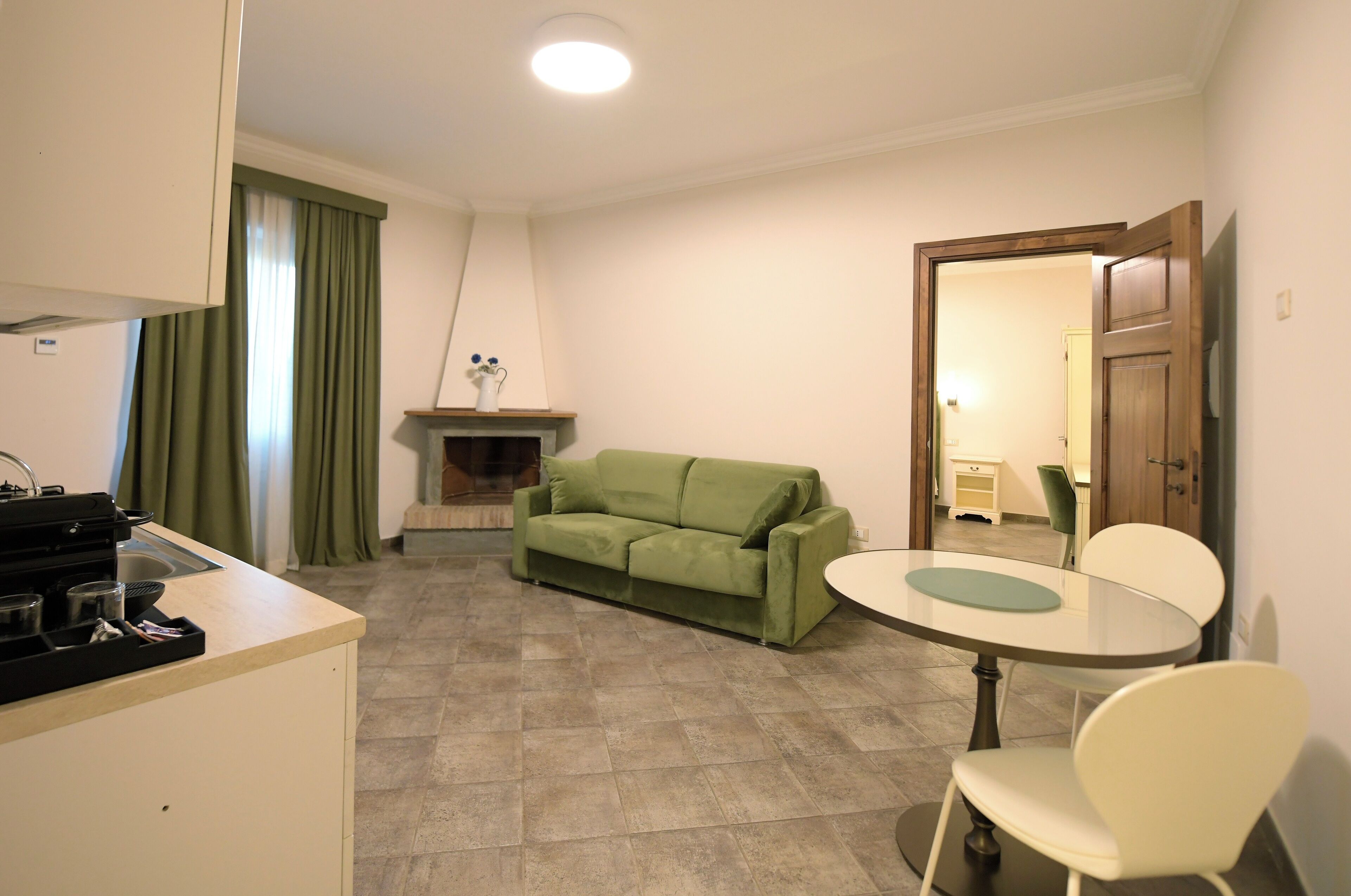 Een knus woongedeelte met een kitchenette, een groene bank, een ronde eettafel en een kleine open haard.