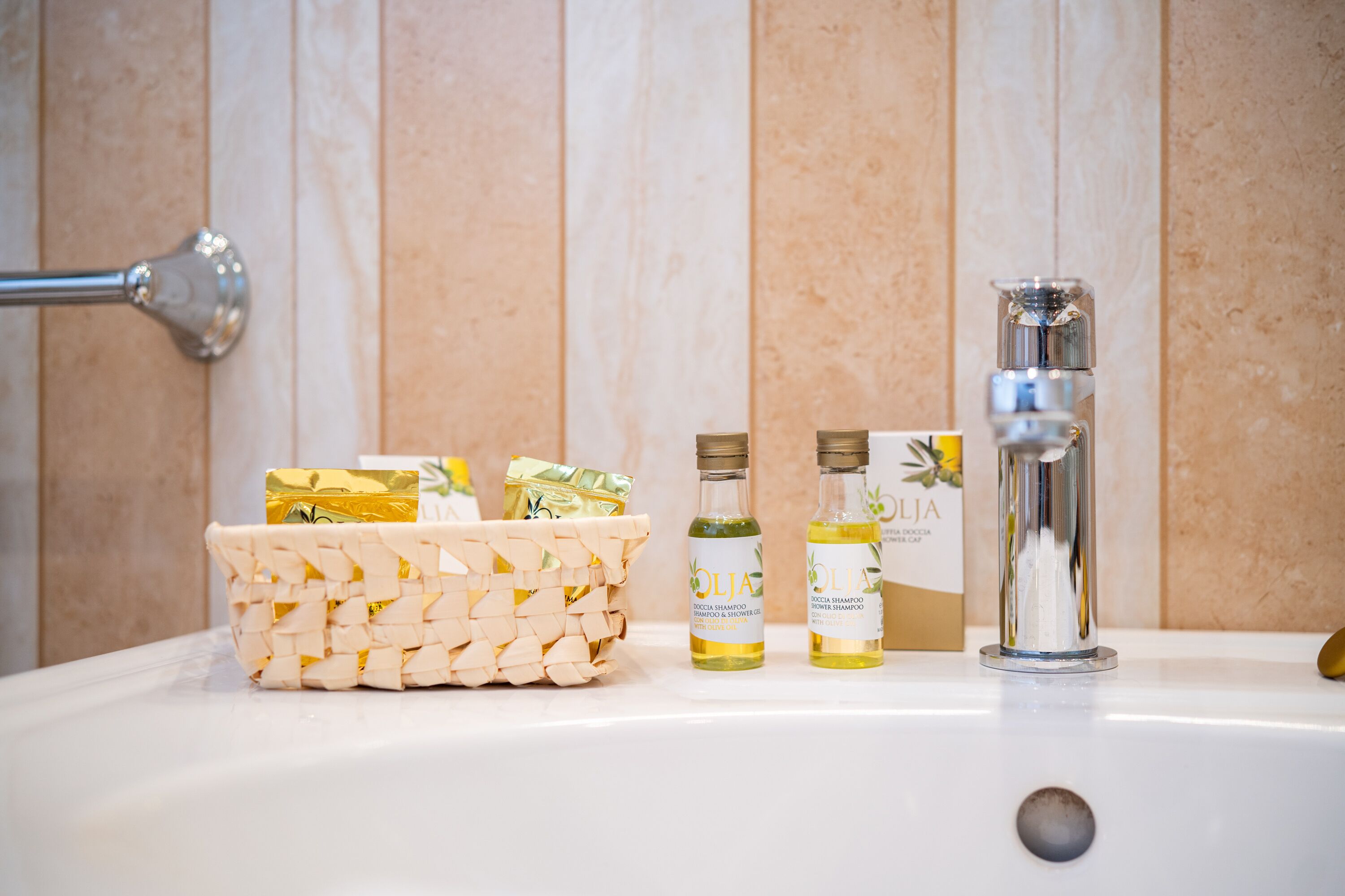 Un lavabo de salle de bain avec un panier en osier contenant des articles de toilette, deux bouteilles de shampoing et un robinet.