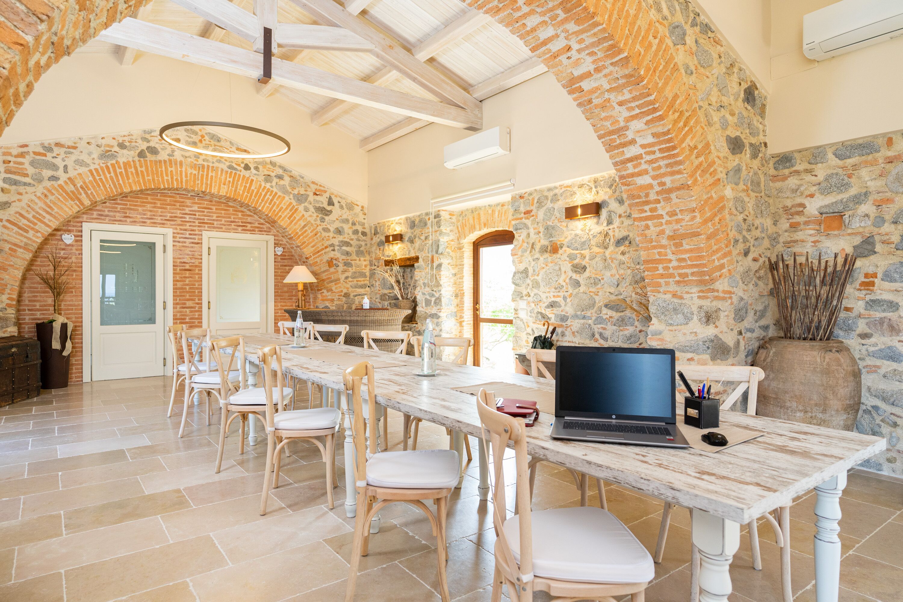 A spacious dining area with a long table, several chairs, and a laptop on the table.
