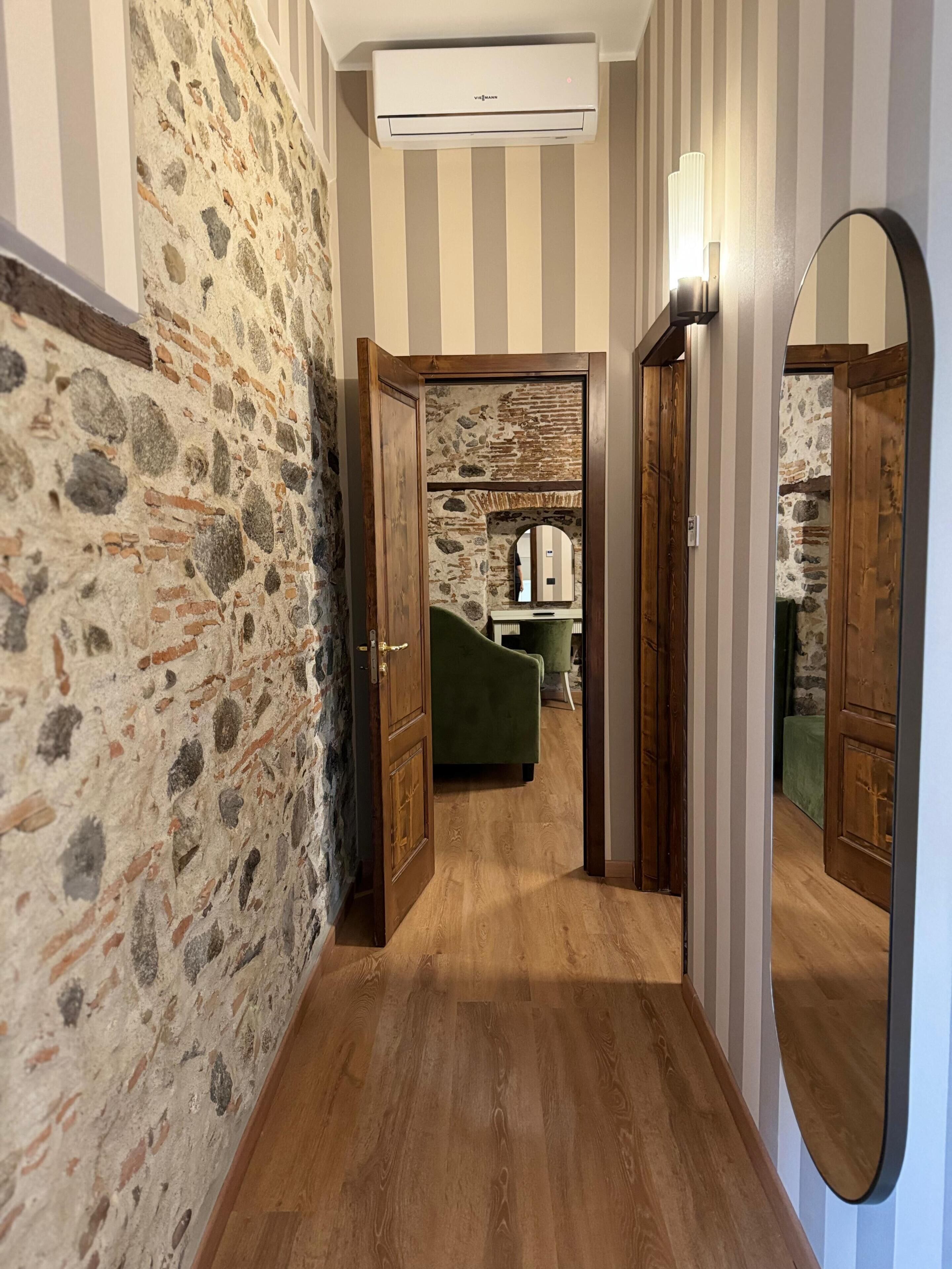 Un pasillo con paredes de piedra, suelo de madera y una puerta espejada.