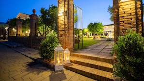 A stone pathway leading to a gated entrance with lanterns, surrounded by greenery and a clear night sky.