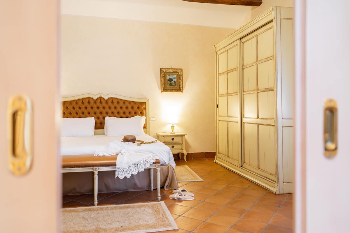 A bedroom with a bed, nightstand, lamp, wardrobe, and a picture on the wall.