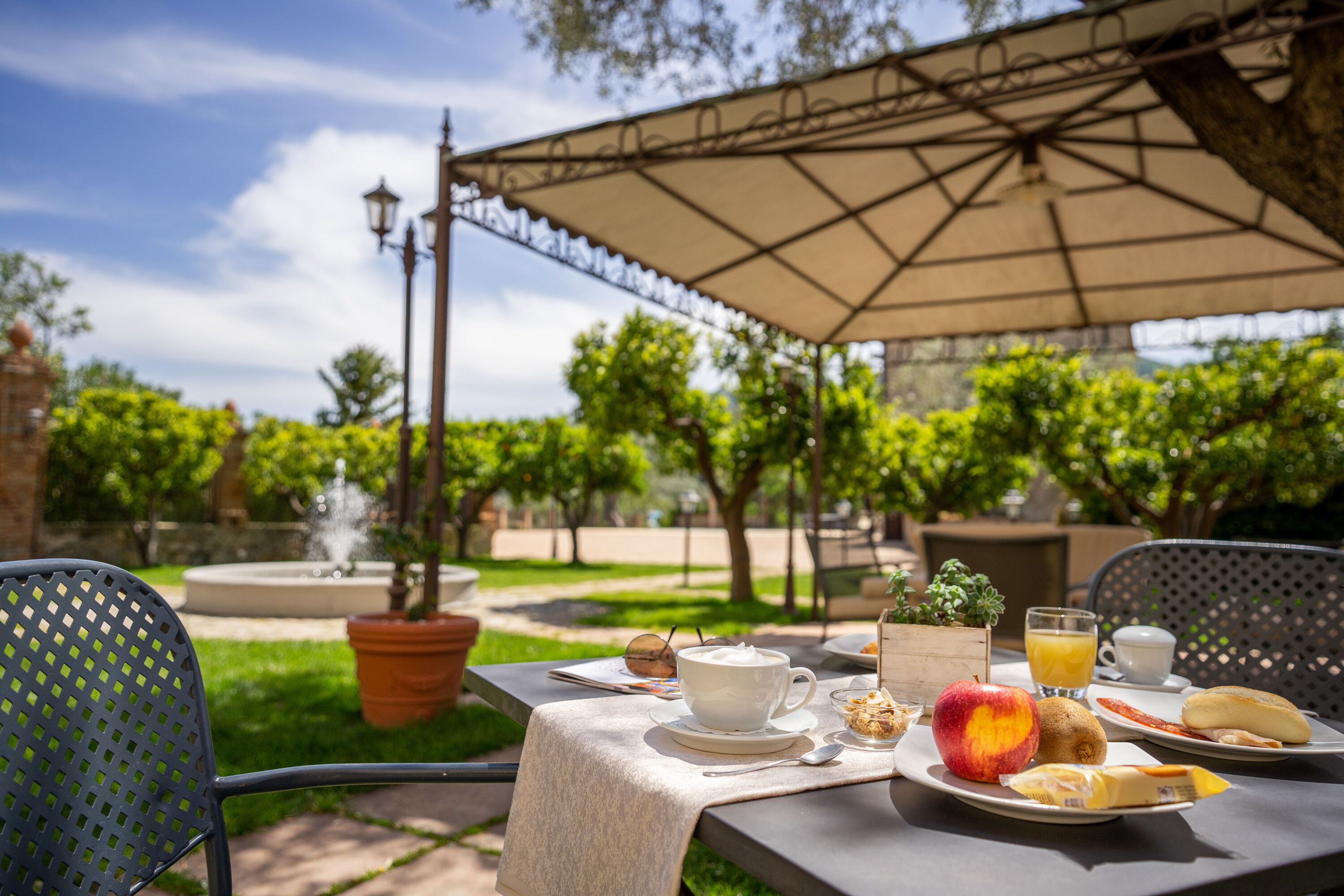 An outdoor dining area with a table set for breakfast, including a cup, a plate with an apple, a banana, and a glass of orange juice.