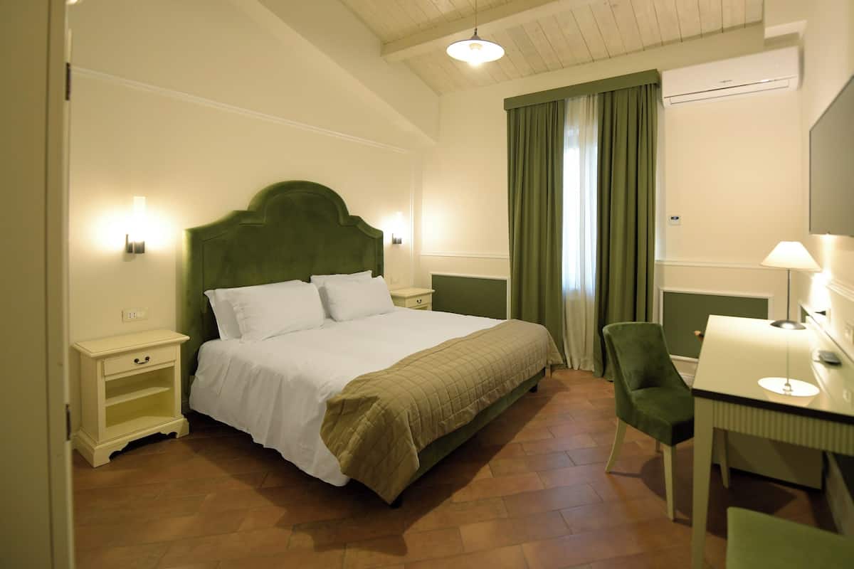 A hotel room with a bed, a desk, a chair, a TV, and a window with curtains.