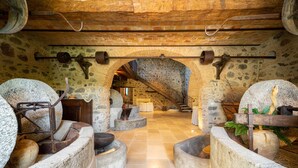 A rustic interior with stone walls, a brick ceiling, and a central staircase. There are stone benches and a large stone basin.