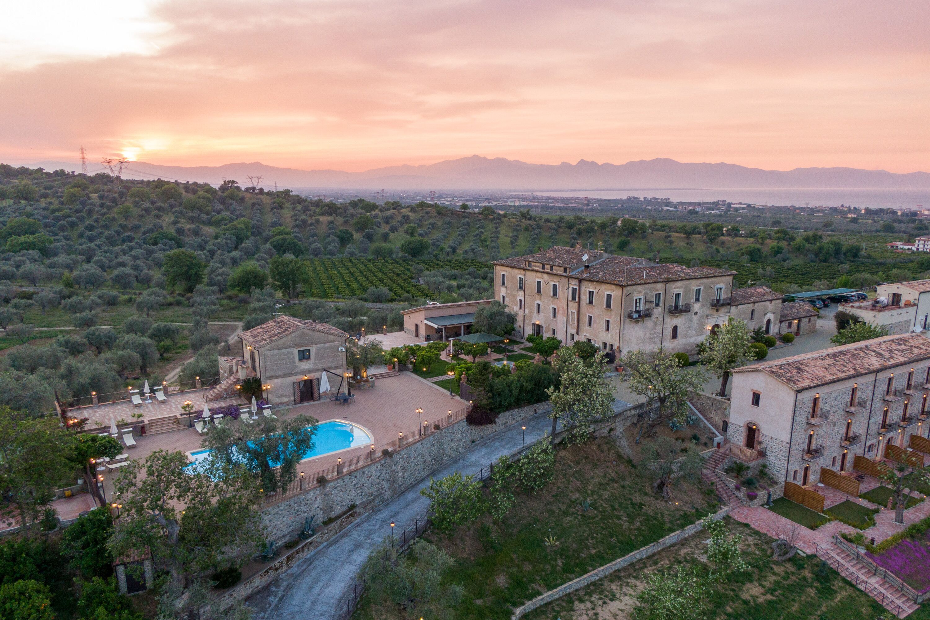 A villa with a swimming pool, surrounded by olive groves and a view of distant mountains.