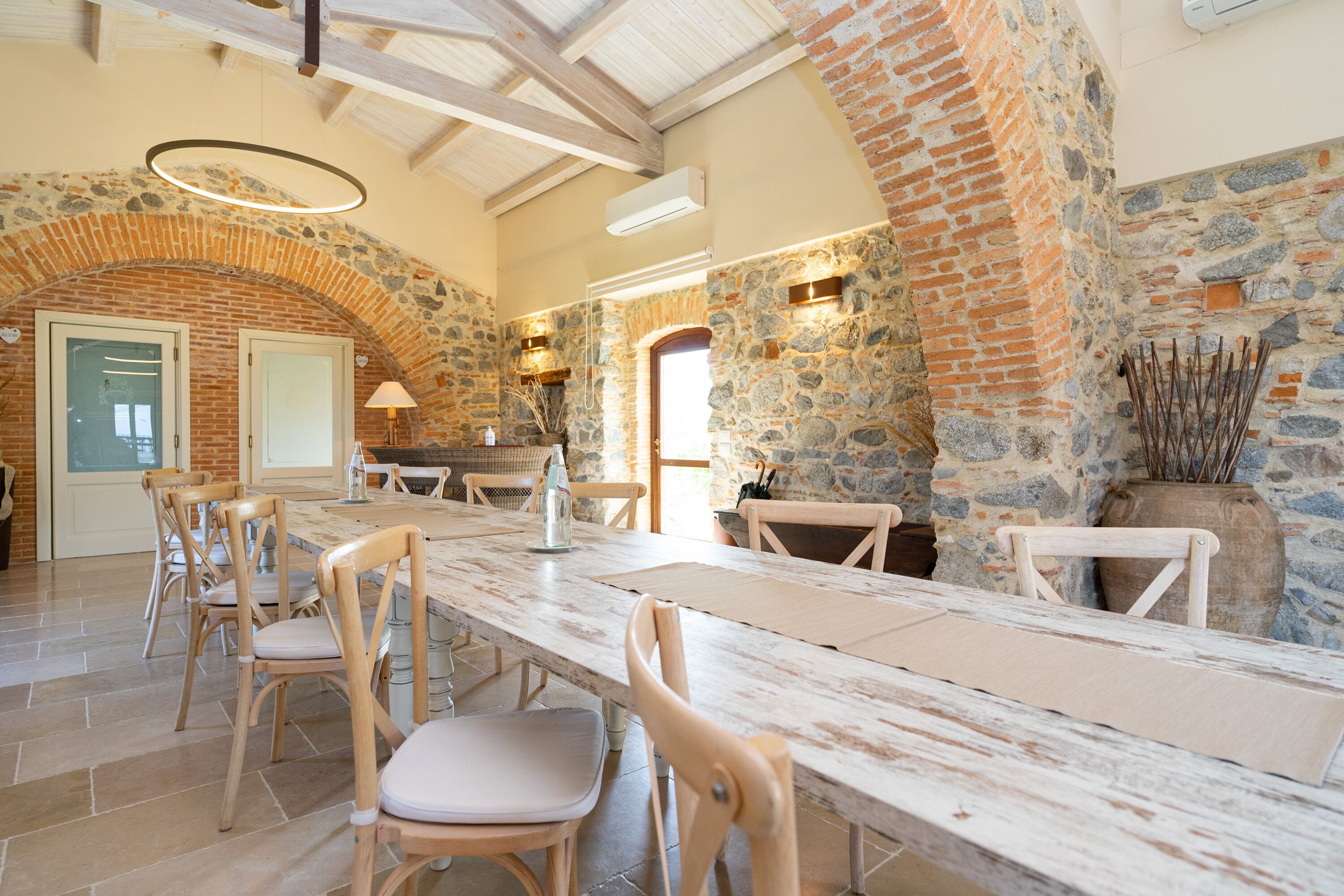 Un comedor espacioso con una larga mesa de madera, varias sillas y un fondo de pared de piedra.