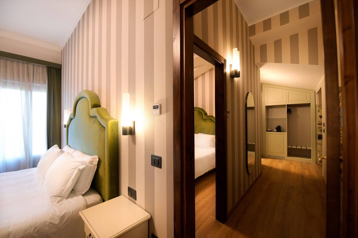 A hotel room with a bed, bedside table, and a mirror reflecting a closet and a bathroom.