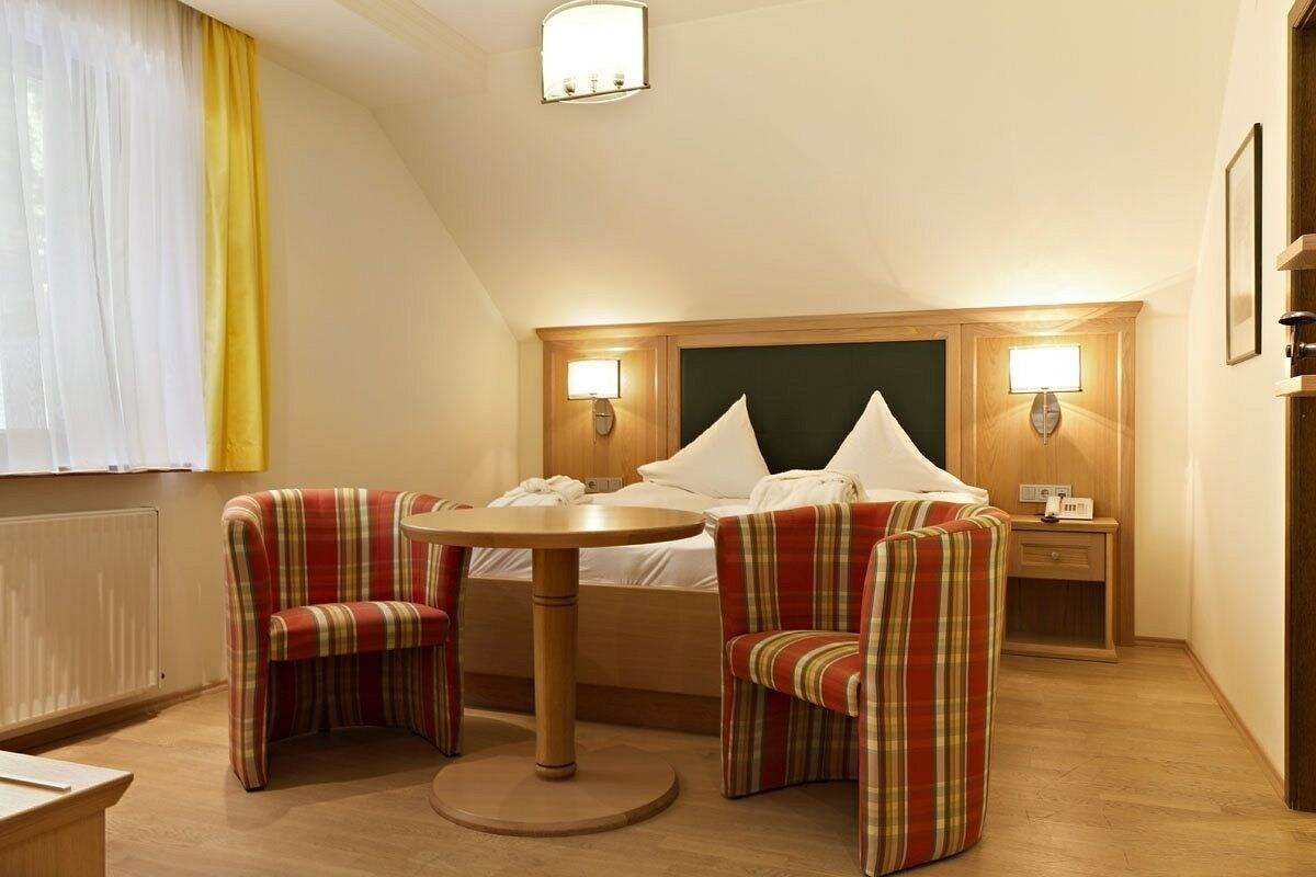 Habitación de hotel con una cama, dos sillones a rayas, una mesa redonda y dos lámparas de noche.