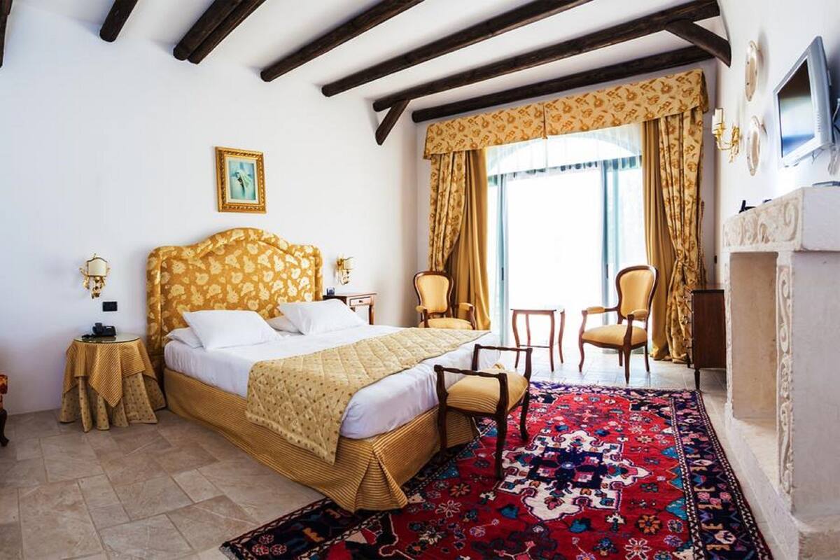 A hotel room with a large bed, a sitting area with a chair, a small table, and a television.