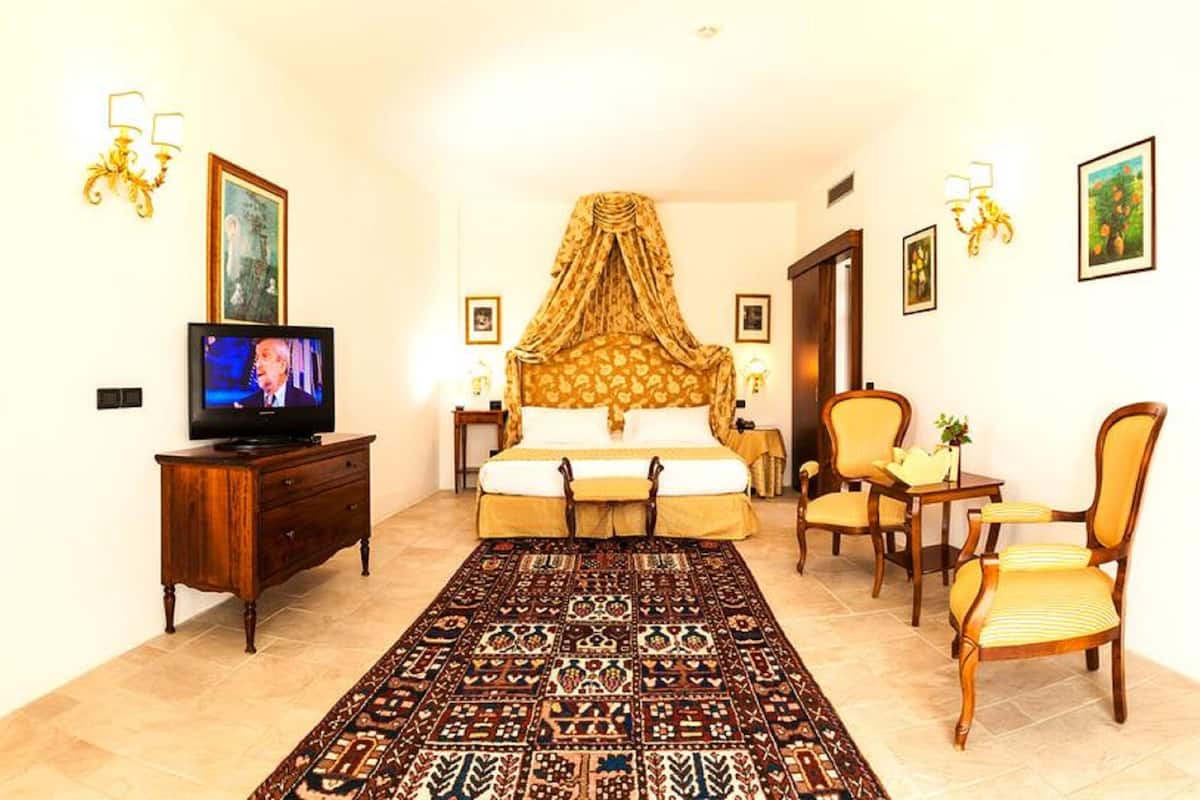 A hotel room with a large bed, a television, a wooden dresser, a patterned rug, and a chair.