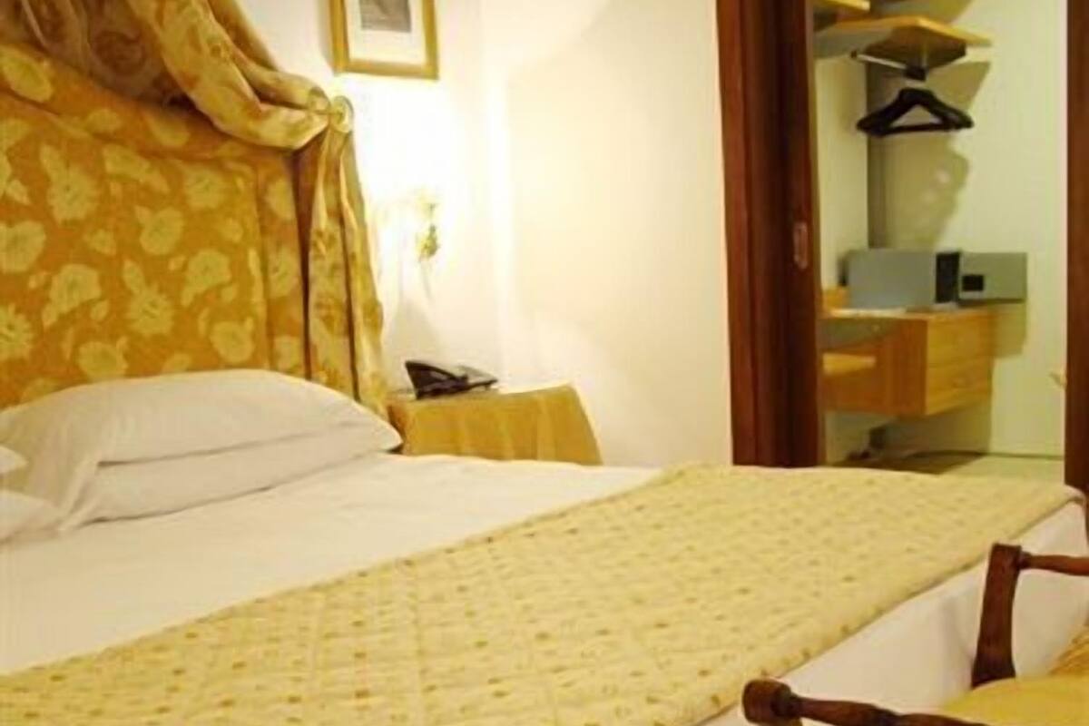 A hotel room with a large bed, a bedside table, a chair, and a wardrobe.