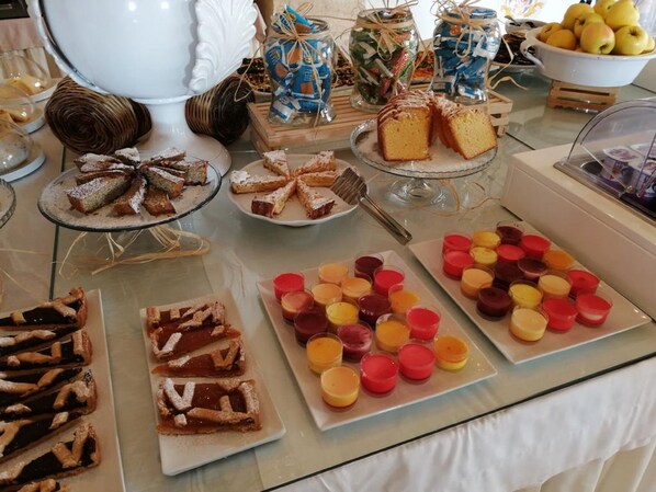 A buffet table with various desserts and pastries, including cakes, tarts, and fruit cups.