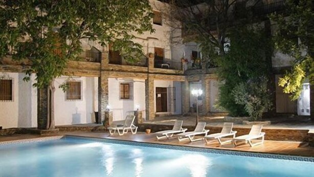 Un área de piscina con sillones de descanso y un edificio con varias ventanas y balcones.