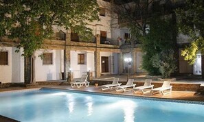 A pool area with lounge chairs and a building with multiple windows and balconies.