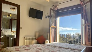 Un dormitorio con cama, televisor, baño y balcón con vistas.