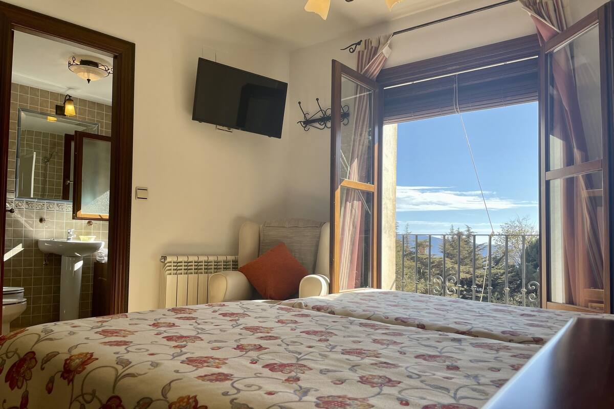 Un dormitorio con cama, televisor, baño y balcón con vistas.