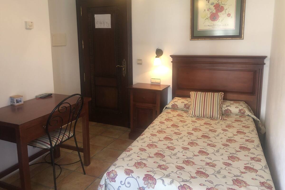 Un dormitorio con cama, mesita de noche, escritorio y silla.