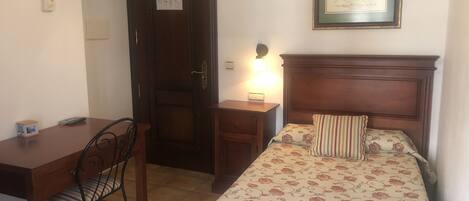Un dormitorio con cama, mesita de noche, escritorio y silla.