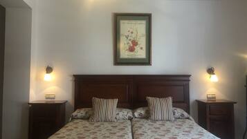 A double bed with floral bedding, two bedside tables, a framed botanical illustration, and wall-mounted lamps.