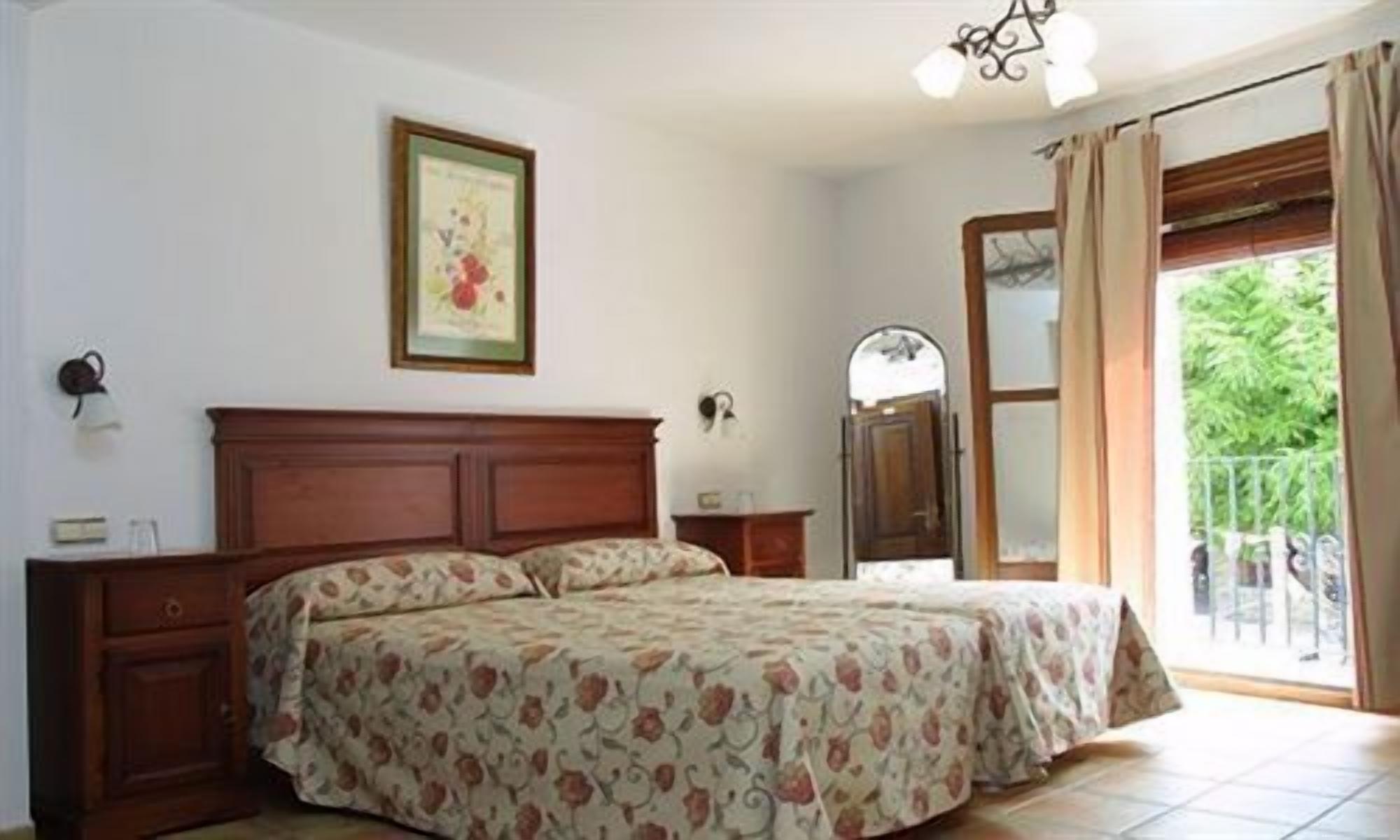 A bedroom with a wooden bed, a nightstand, a mirror, and a window with curtains.