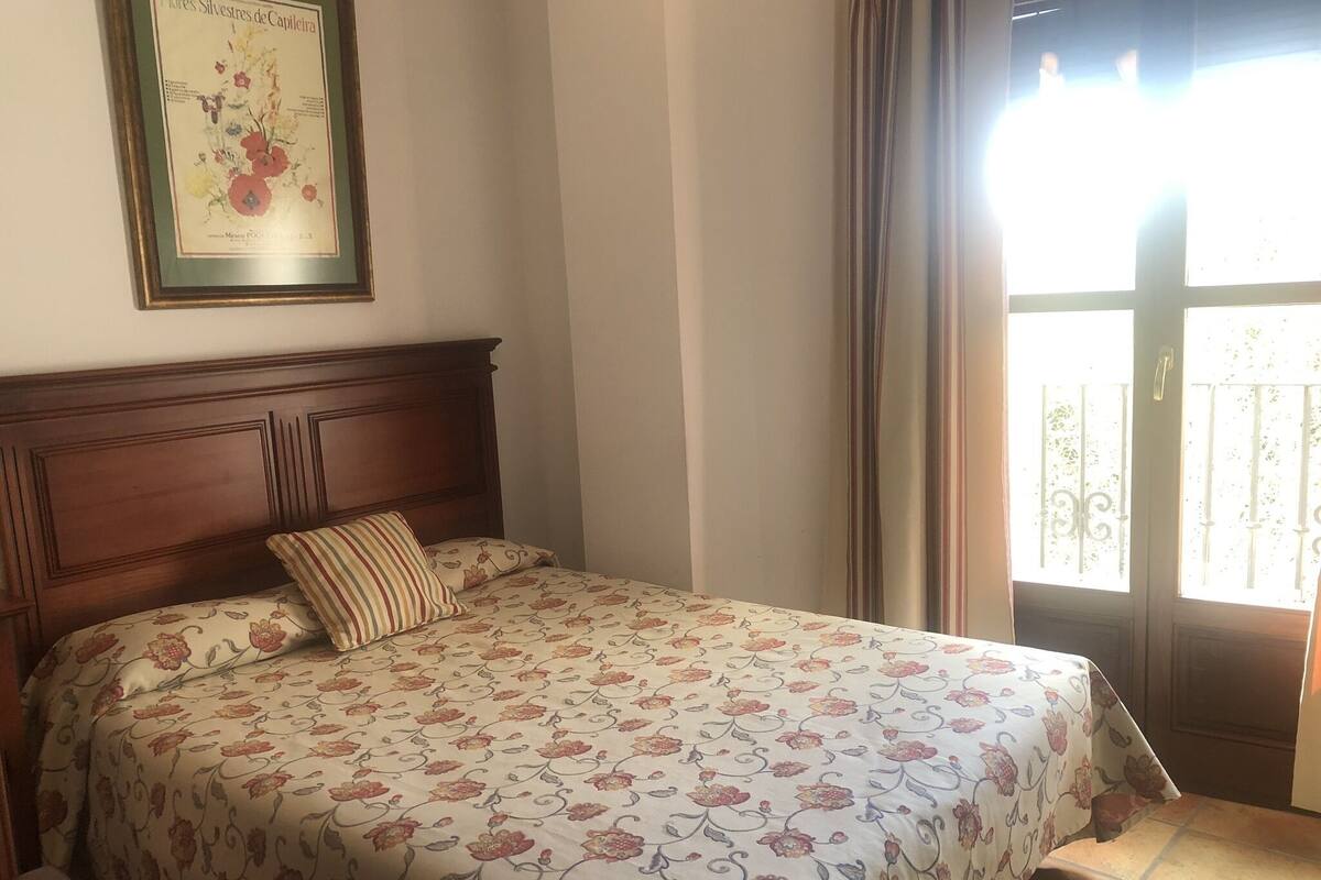 Un dormitorio con cabecera de madera, colcha con estampado floral e ilustración botánica enmarcada en la pared.