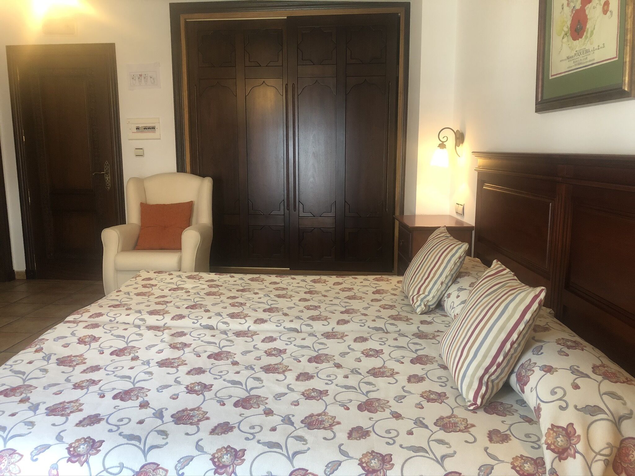 Een slaapkamer met een groot bed, een stoel, een kledingkast en een lijst met een afbeelding aan de muur.
