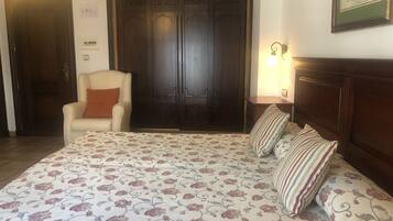 Een slaapkamer met een groot bed, een stoel, een kledingkast en een lijst met een afbeelding aan de muur.