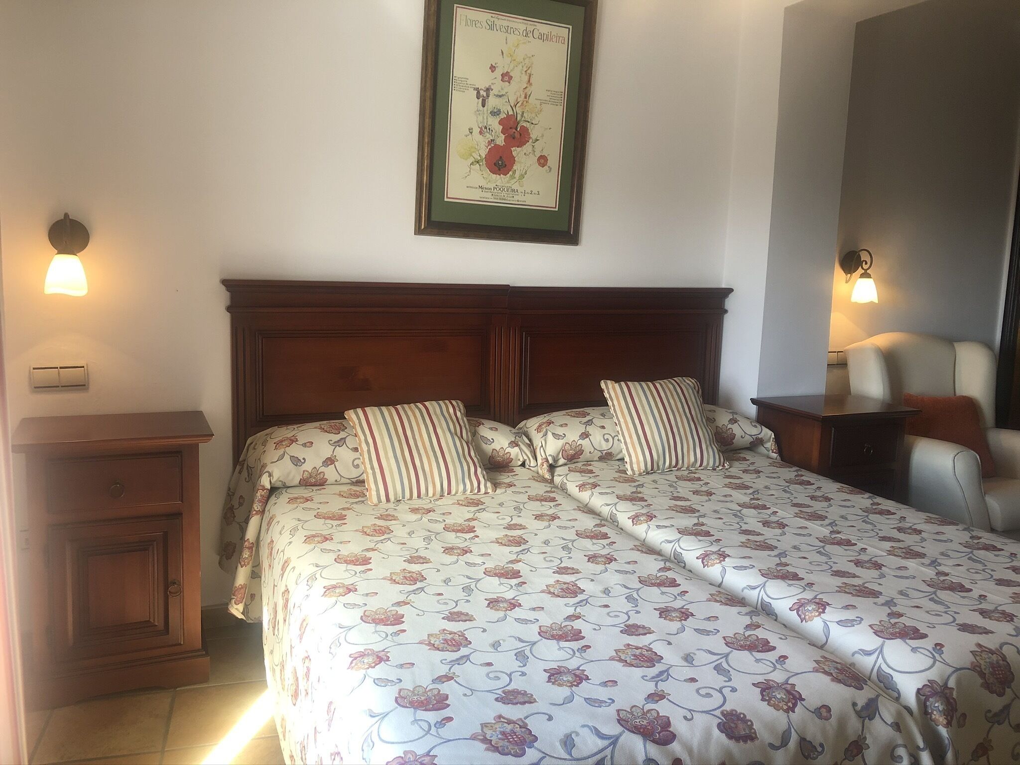 Ein Doppelbett mit Blumenmuster-Bettwäsche, ein Holz-Kopfteil, Nachttische und ein gerahmtes Pflanzenbild an der Wand.