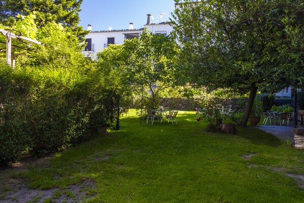 A garden with a table and chairs, a building in the background, and a clear sky.
