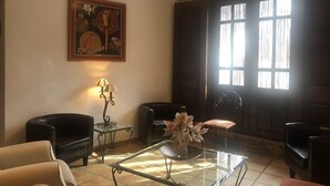 Una sala de estar con una mesa de centro de vidrio, dos sillones, una lámpara y un cuadro en la pared.