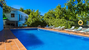 Relax by the serene pool surrounded by lush greenery and a clear sky.