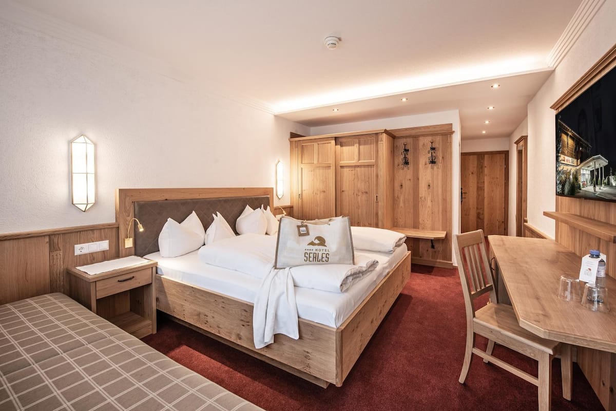 A hotel room with a wooden bed, a small desk, a chair, and a dining table.