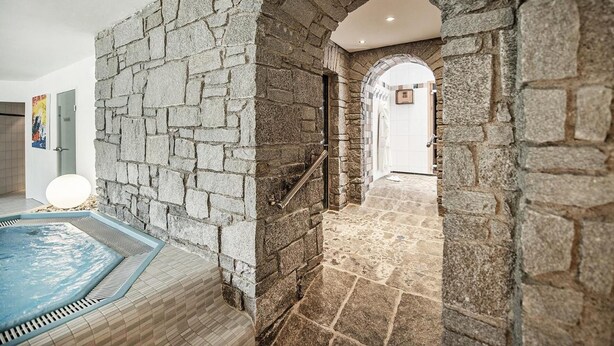A stone-walled indoor pool area with a clear pathway leading to a door. - Hotel Serles (Mieders)