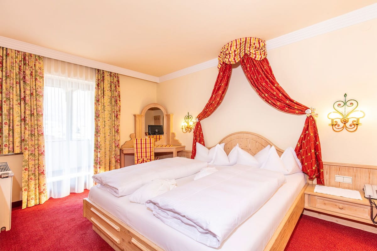 A hotel room with a large bed, a desk with a chair, a mirror, and a telephone.