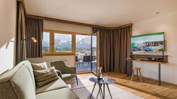 Una sala de estar moderna con un sofá, una mesa de centro, un televisor y vistas a montañas a través de amplios ventanales.