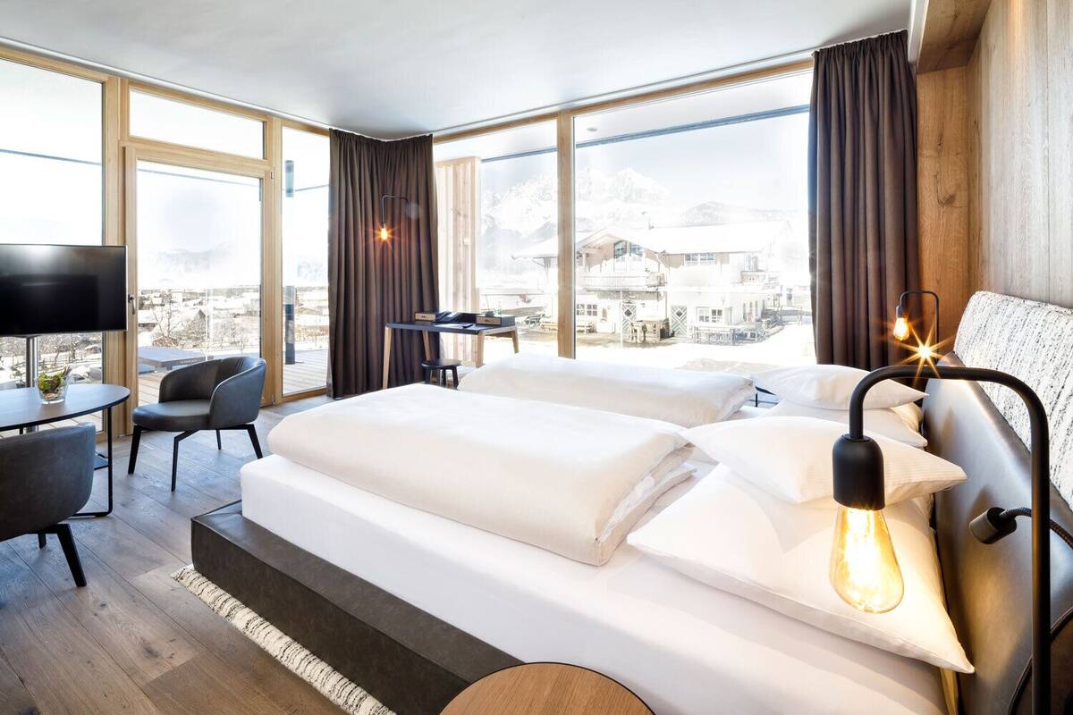 A modern hotel room with a large bed, a desk, a chair, and a TV.