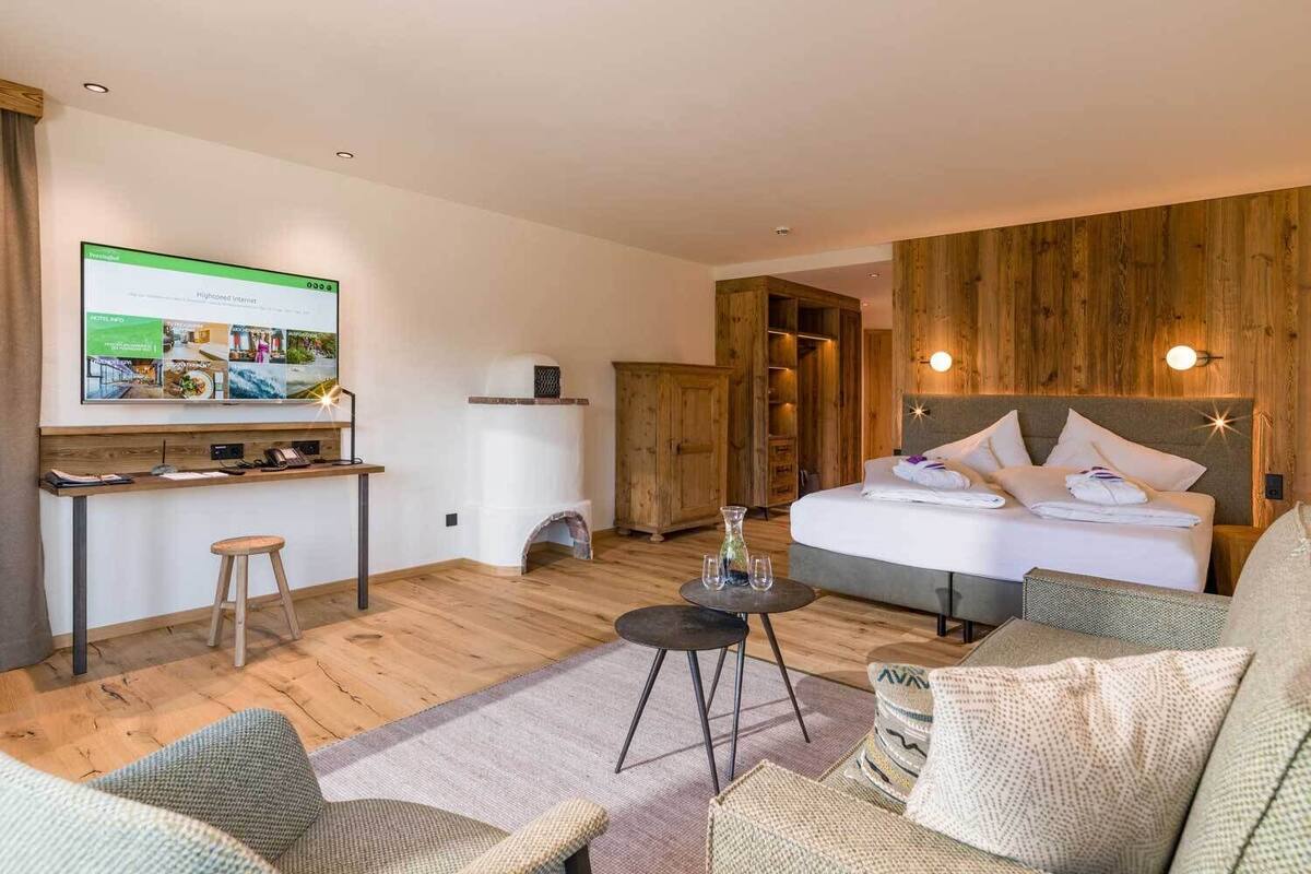 A hotel room with a bed, a desk with a computer, a TV, and a wooden wall.