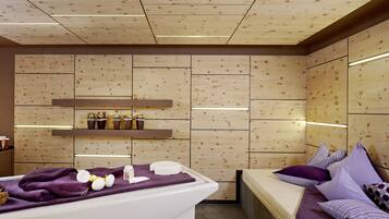 A modern spa room with a wooden panel wall, a white bathtub, and a bed with purple bedding.