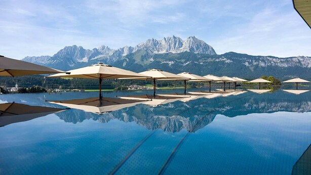 Una piscina infinita con sombrillas y un telón de fondo montañoso.