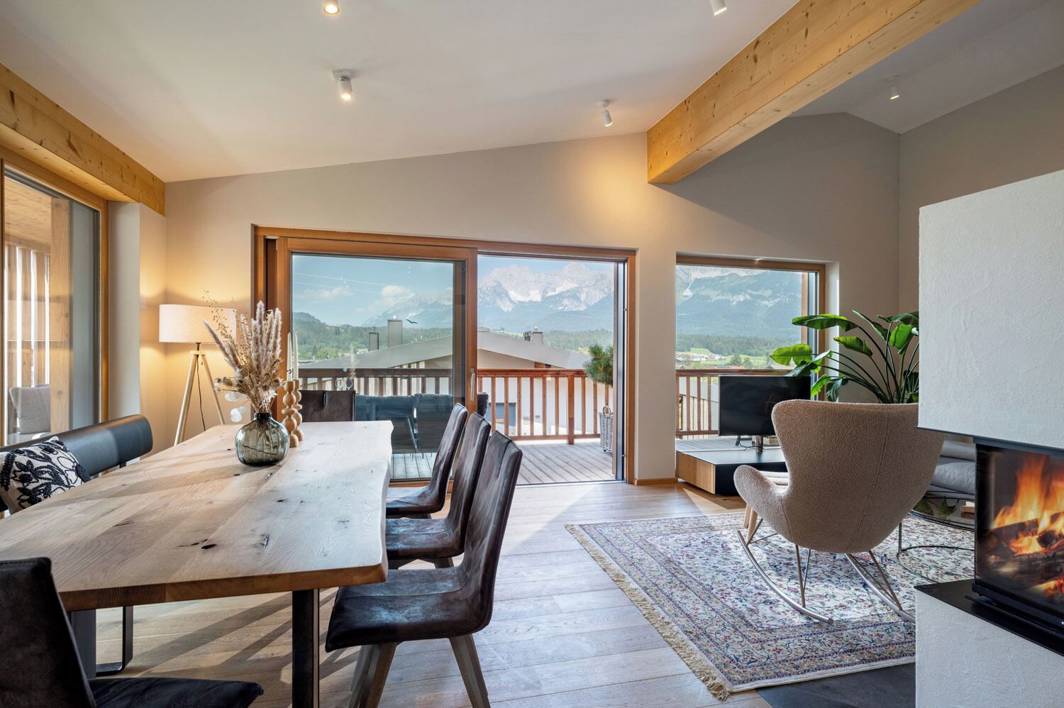Ein modernes Wohnzimmer mit Essbereich, großen Fenstern und Bergblick.