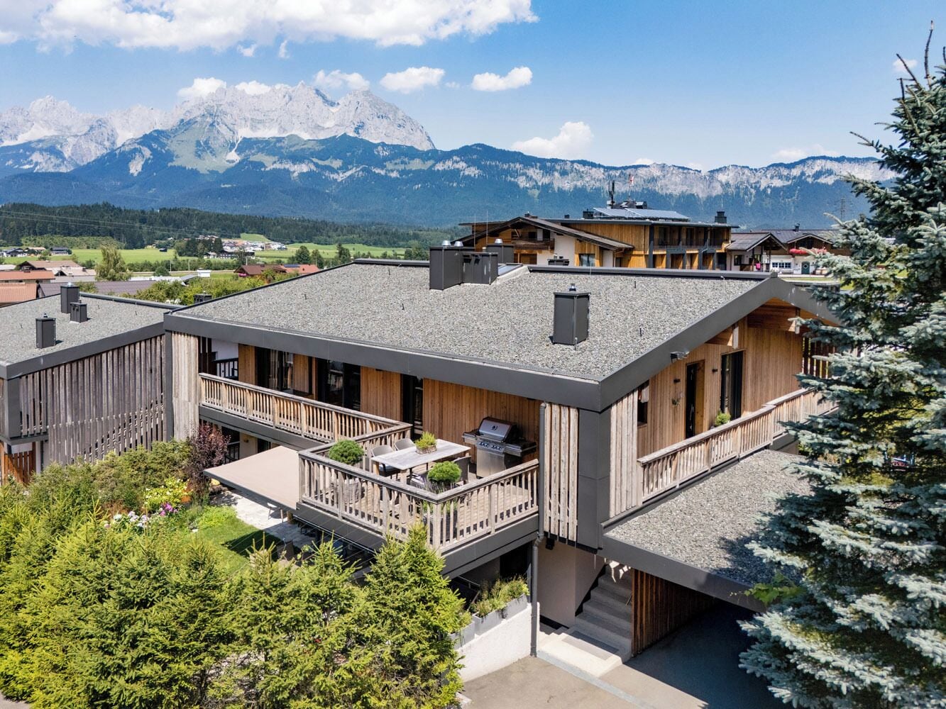 A modern two-story house with a balcony, a barbecue area, and a view of mountains.