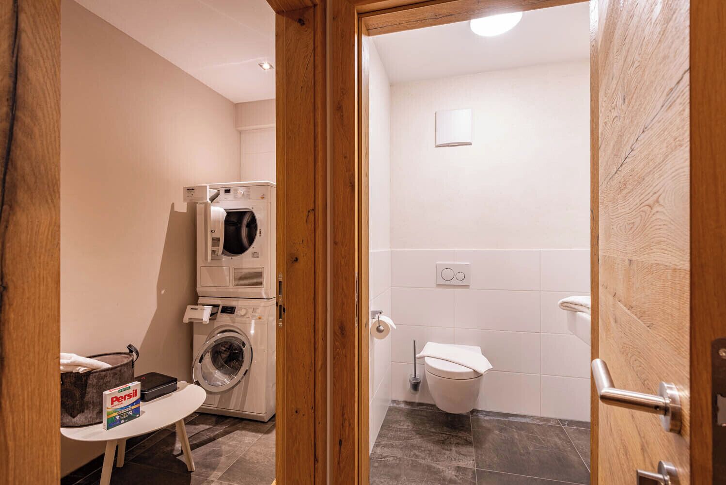 A compact bathroom with a washing machine, a toilet, and a small sink.